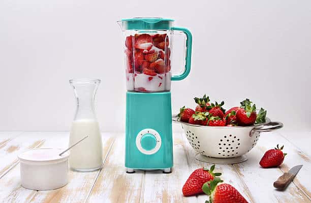 Blender bleu avce fraises et crème à l'intérieur pour faire un milkshake rapide