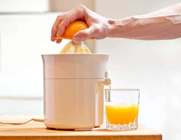 Homme en train de faire du jus d'orange avec un presse-agrume électrique